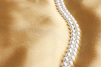 Photo of Beautiful pearl necklace on golden silk, closeup. Space for text