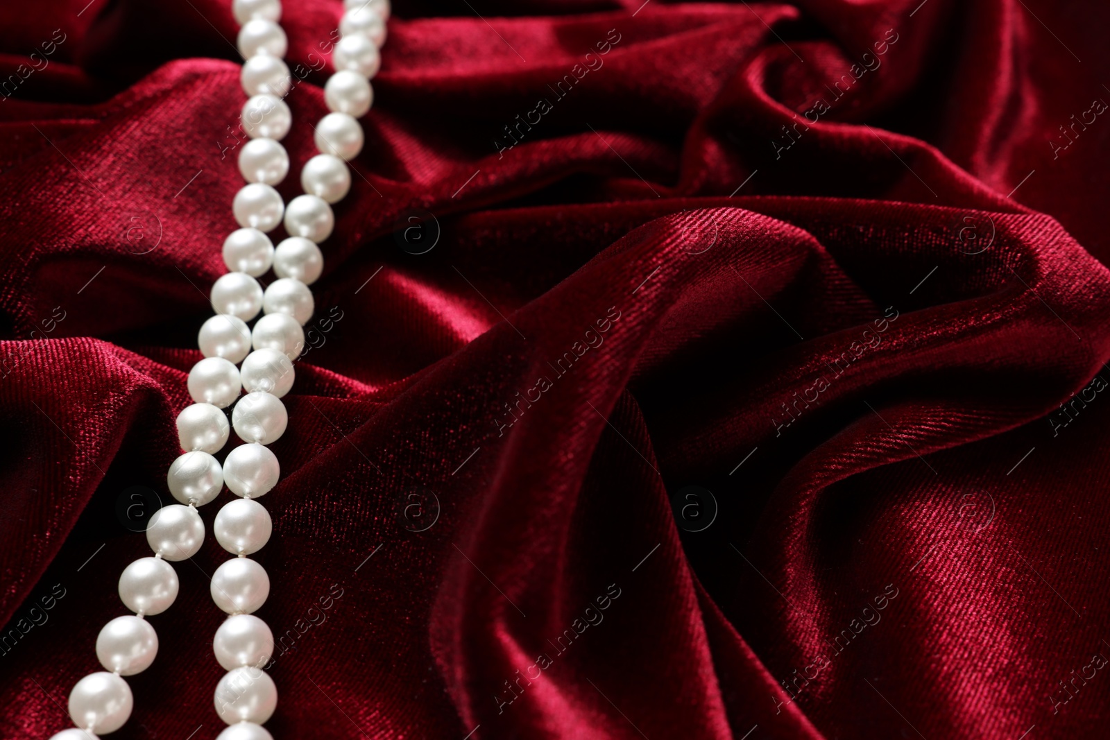 Photo of Beautiful pearl necklace on red cloth, above view. Space for text