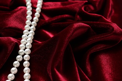 Photo of Beautiful pearl necklace on red cloth, above view. Space for text