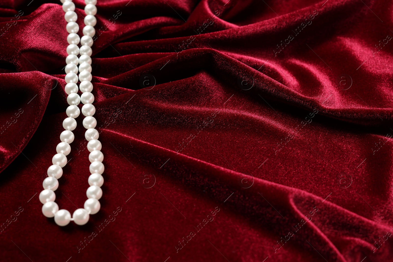 Photo of Beautiful pearl necklace on red cloth, above view. Space for text