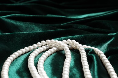 Photo of Beautiful pearl necklace on green cloth, closeup