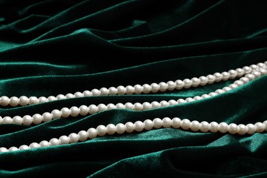 Photo of Beautiful pearl necklace on green cloth, closeup