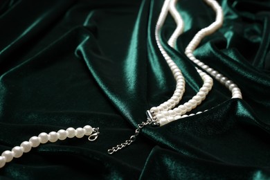 Photo of Beautiful pearl necklace on green cloth, closeup