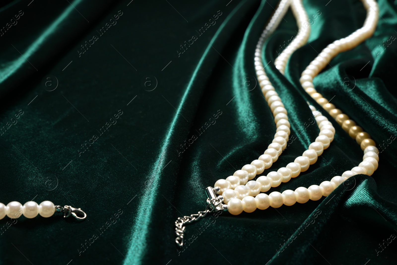 Photo of Beautiful pearl necklace on green cloth, closeup. Space for text