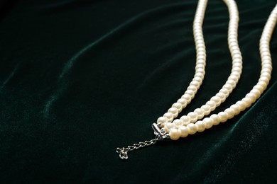 Photo of Beautiful pearl necklace on green cloth, closeup. Space for text