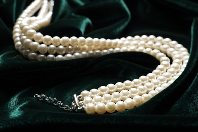 Photo of Beautiful pearl necklace on green cloth, closeup