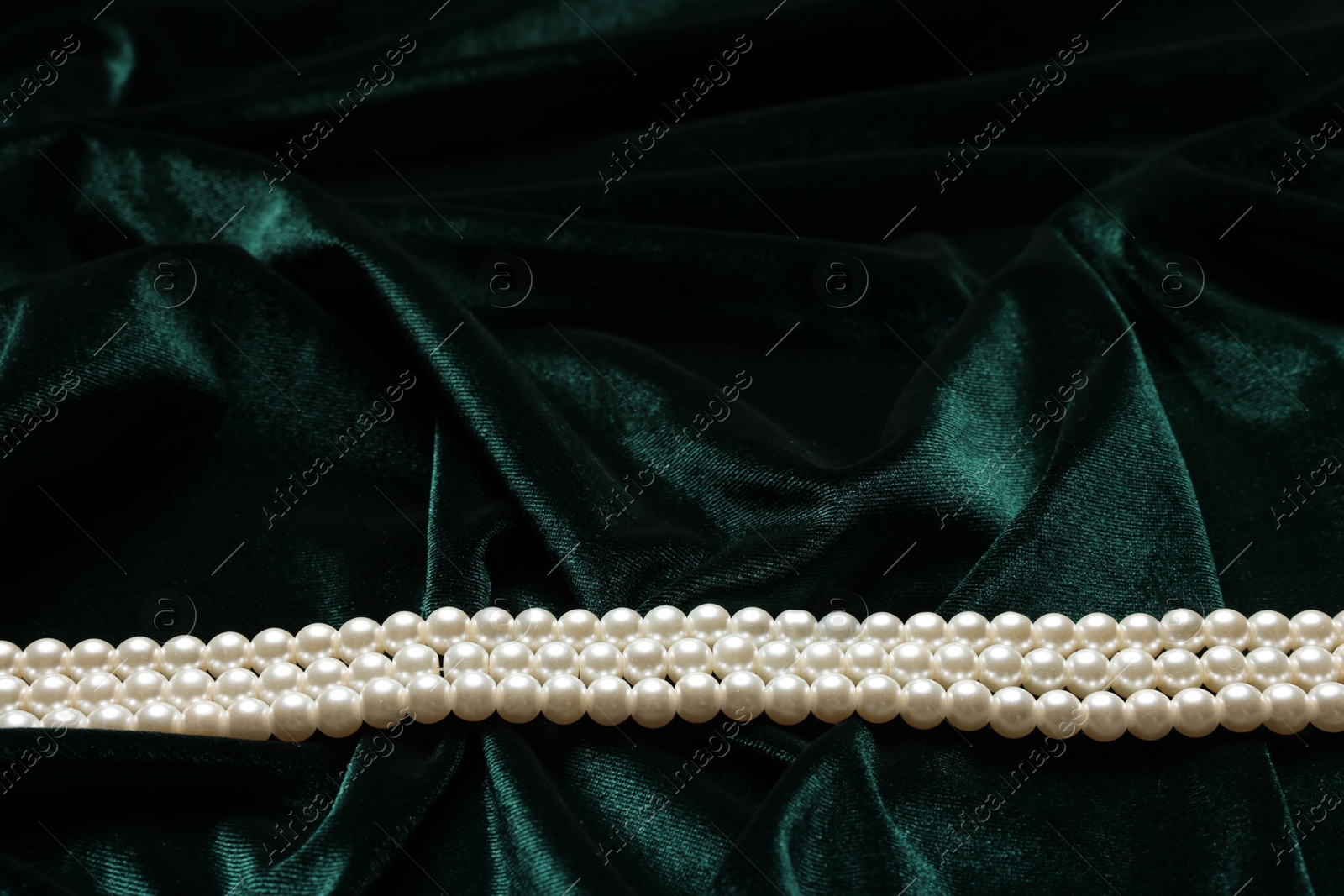 Photo of Beautiful pearl necklace on green cloth, above view. Space for text