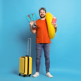 Traveller with passport, ticket, suitcase and beach accessories on light blue background