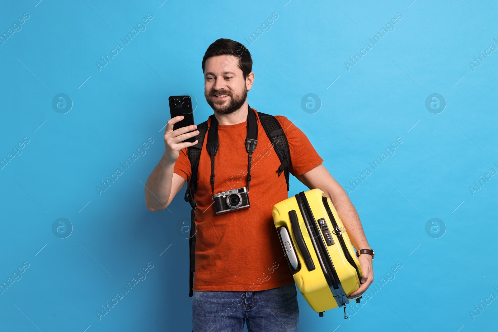 Photo of Traveller with suitcase using smartphone on light blue background