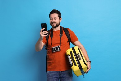 Photo of Traveller with suitcase using smartphone on light blue background