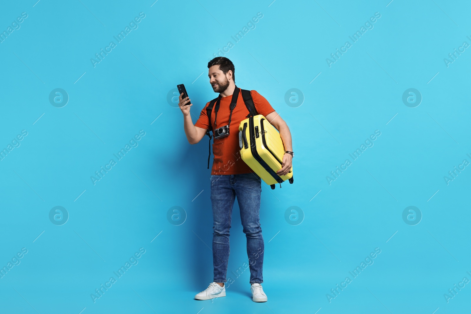 Photo of Traveller with suitcase using smartphone on light blue background