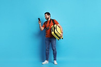 Photo of Traveller with suitcase using smartphone on light blue background