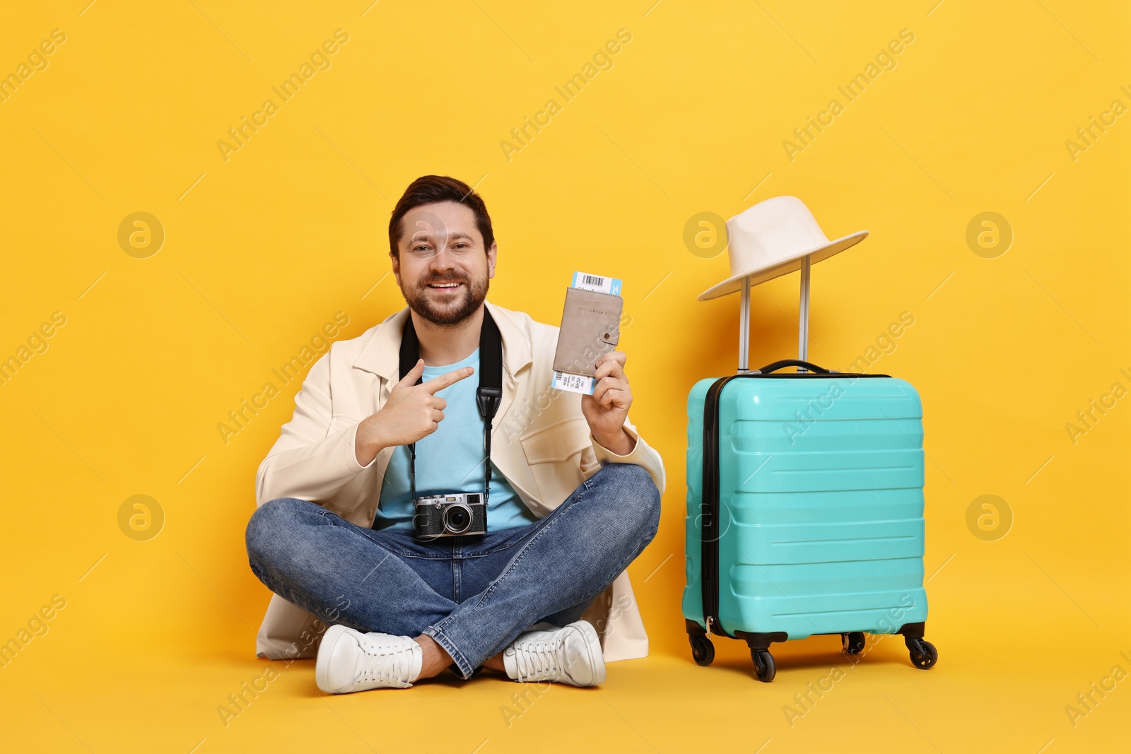 Photo of Traveller with vintage camera, passport, ticket and suitcase on orange background