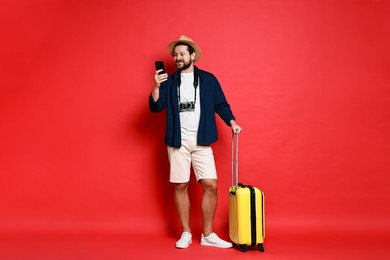 Photo of Traveller with suitcase using smartphone on red background