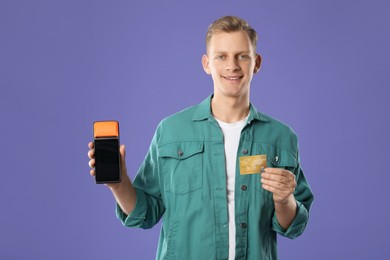 Photo of Happy young man with payment terminal and debit card on purple background