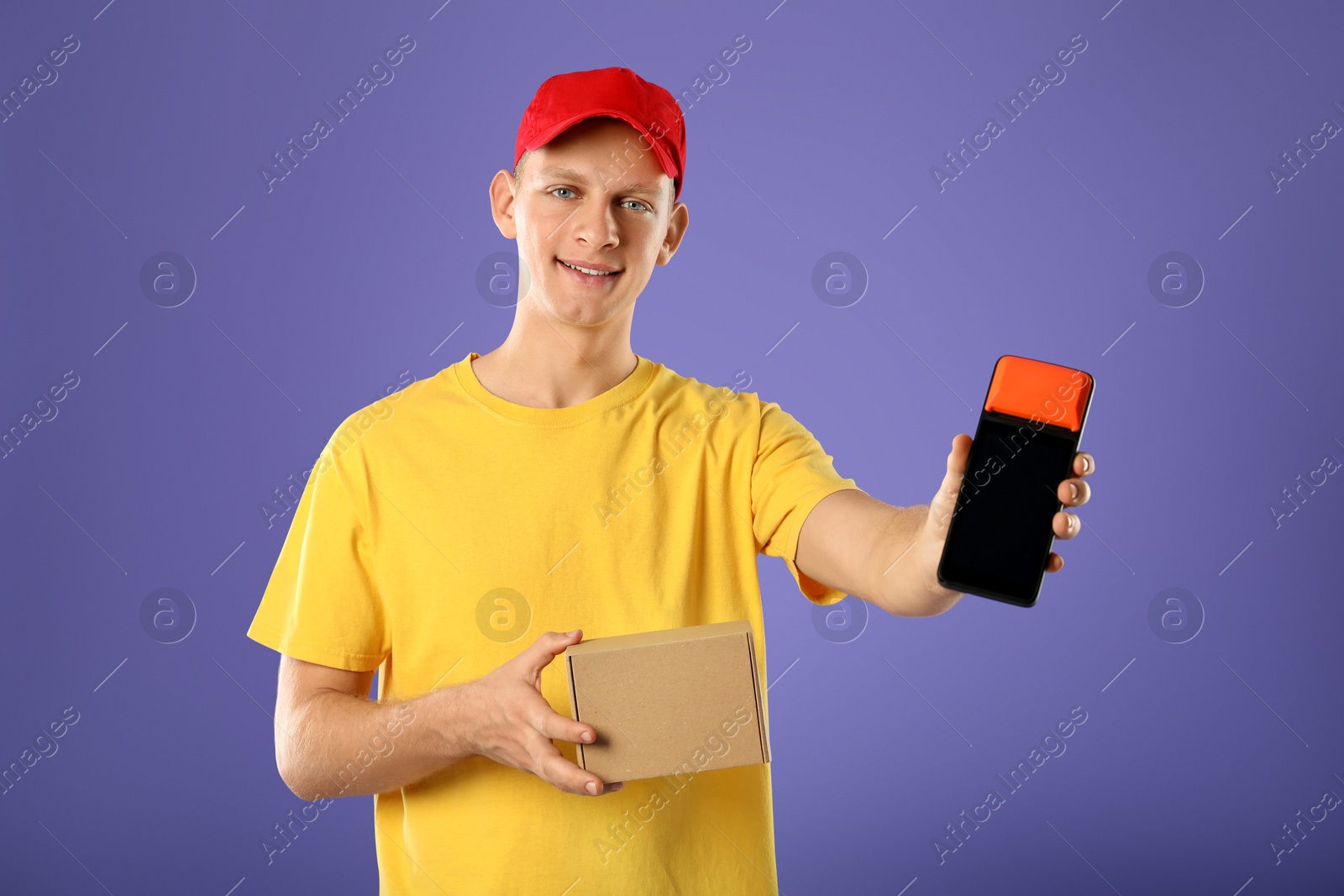 Photo of Happy young courier with payment terminal and parcel on purple background