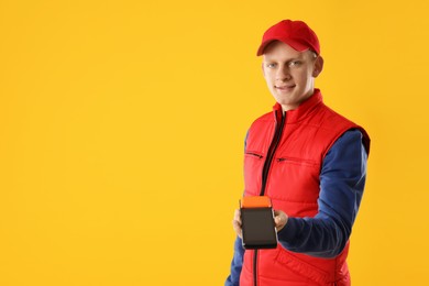 Photo of Happy courier with payment terminal on yellow background, space for text