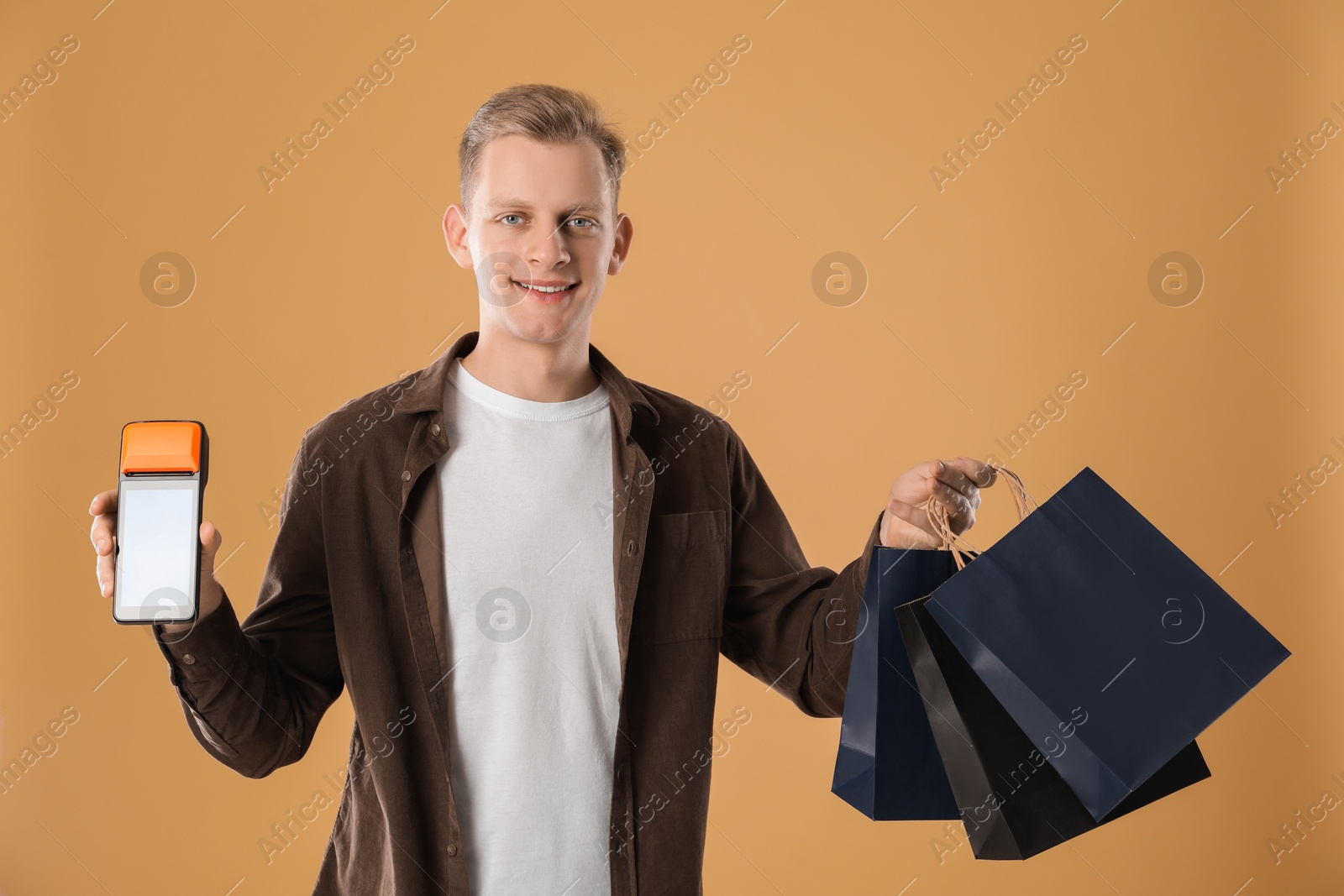 Photo of Happy young man with payment terminal and shopping bags on beige background