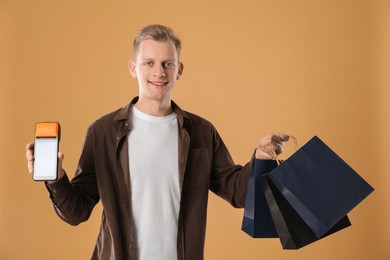 Photo of Happy young man with payment terminal and shopping bags on beige background