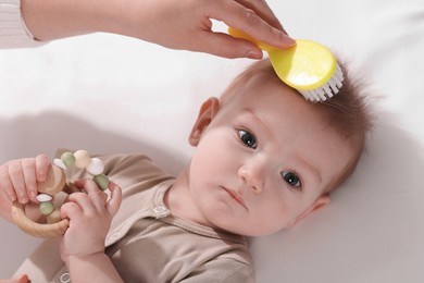 Photo of Woman brushing hair of her little baby indoors, above view