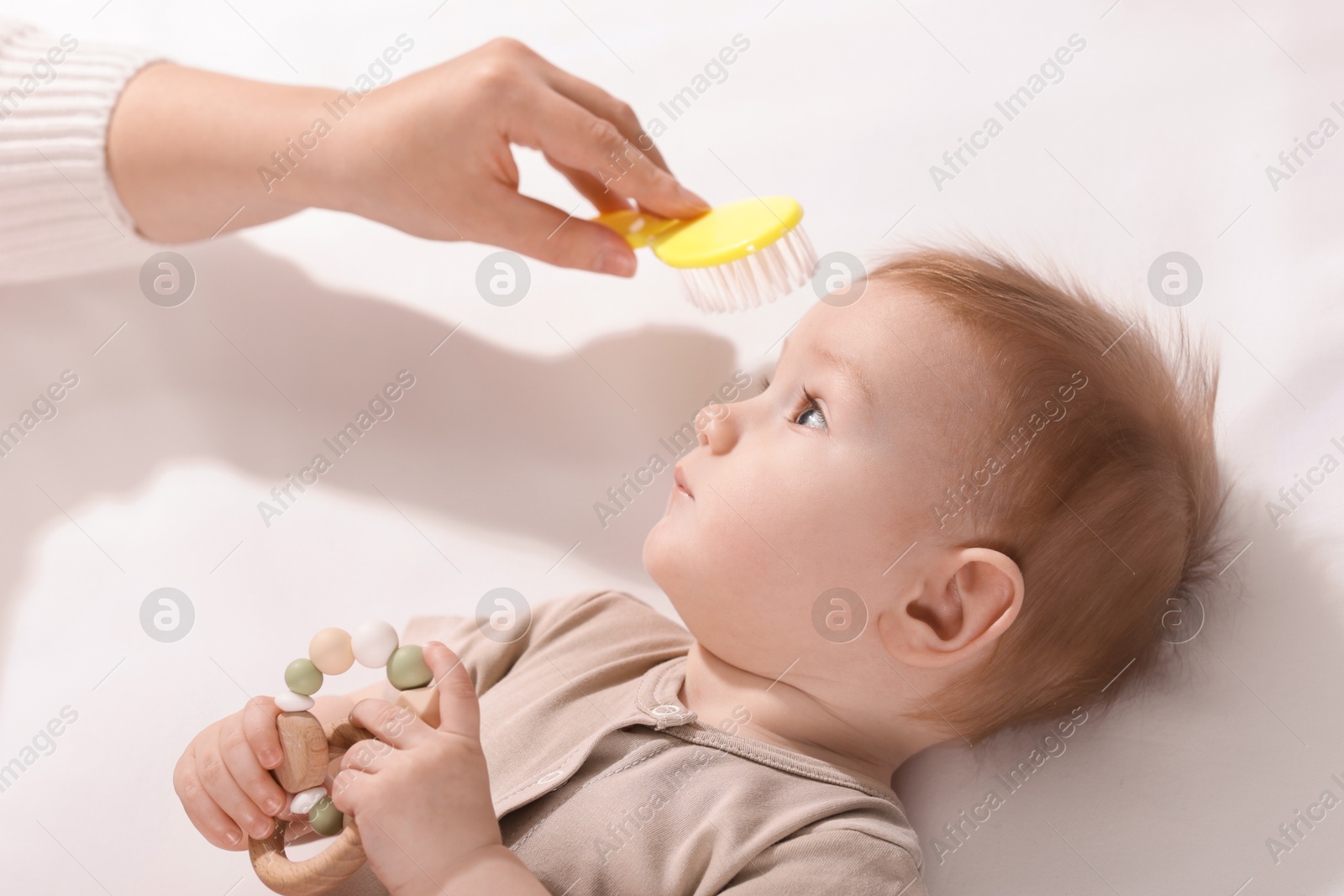 Photo of Woman brushing hair of her little baby indoors, above view