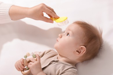 Photo of Woman brushing hair of her little baby indoors, above view