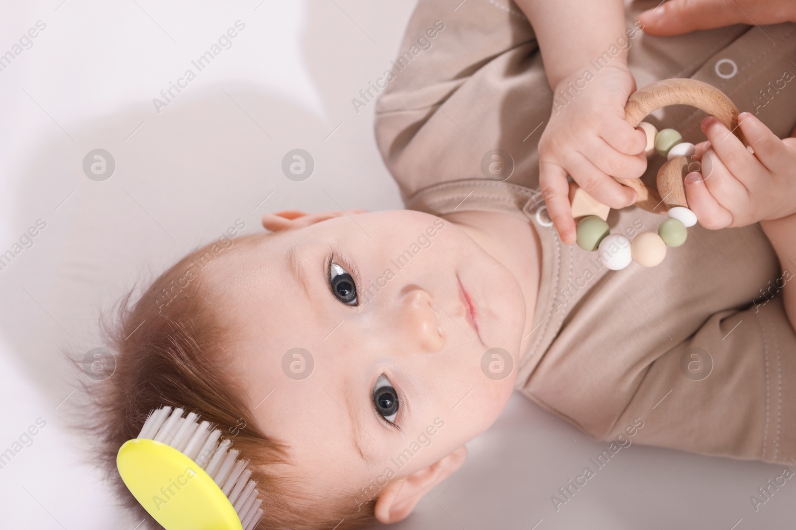 Photo of Parent brushing hair of little baby indoors, above view