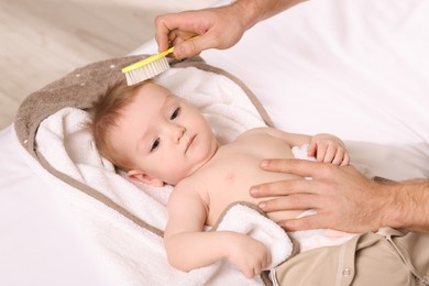 Photo of Man brushing hair of his little baby indoors, closeup