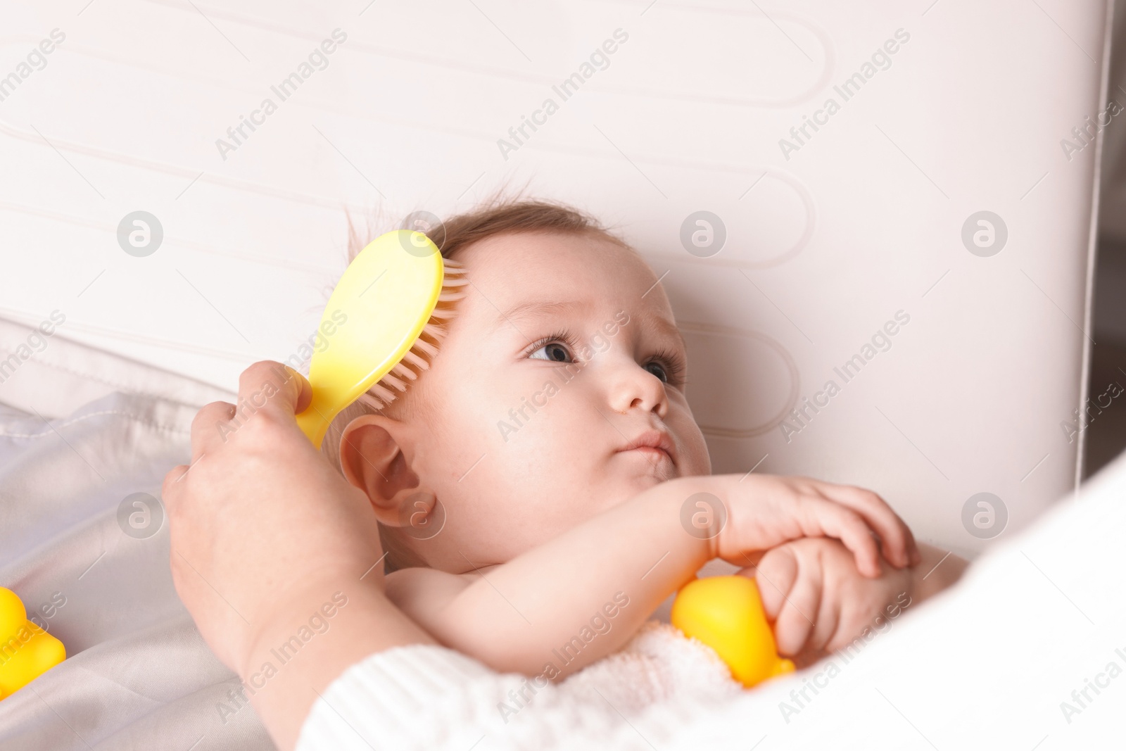 Photo of Woman brushing hair of her little baby indoors, closeup