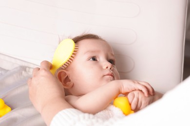 Photo of Woman brushing hair of her little baby indoors, closeup