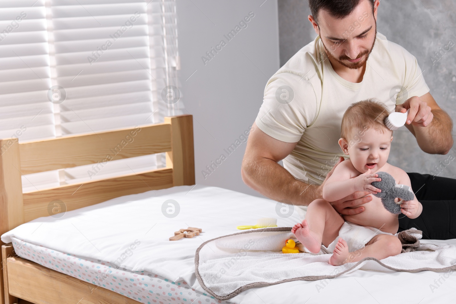 Photo of Man brushing hair of his little baby on bed indoors, space for text