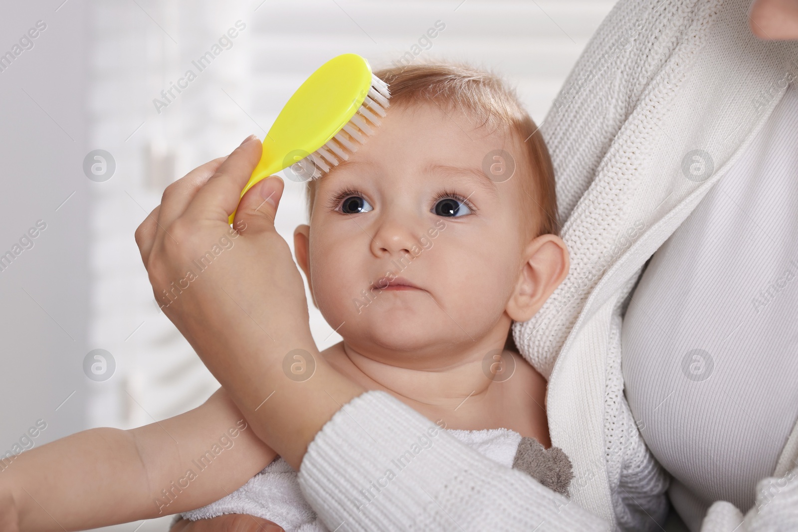 Photo of Woman brushing hair of her little baby indoors, closeup