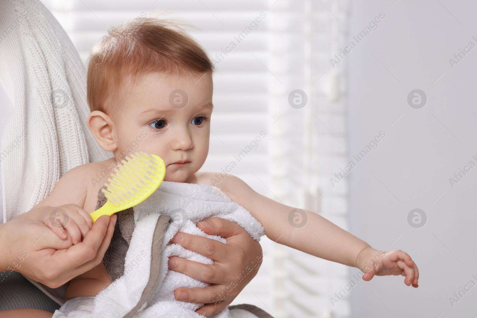 Photo of Woman brushing hair of her little baby indoors, closeup. Space for text