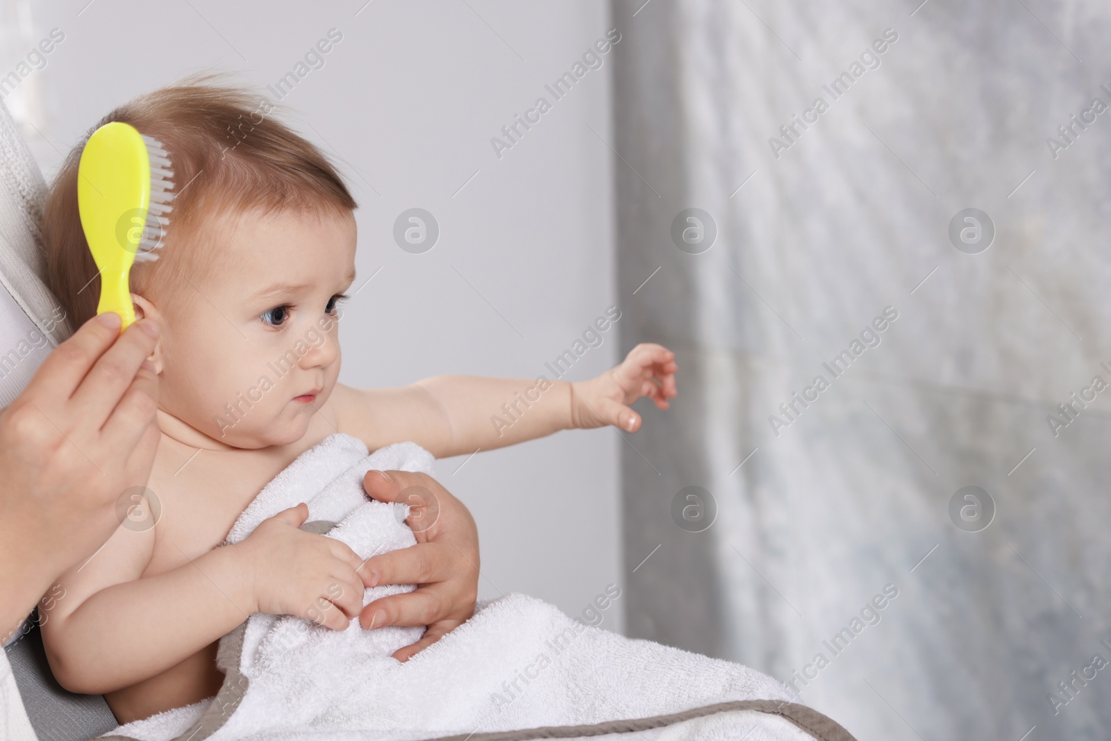 Photo of Woman brushing hair of her little baby indoors, closeup. Space for text