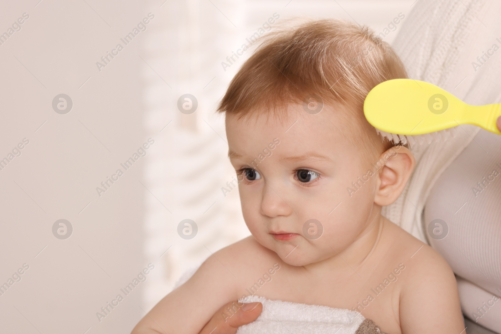 Photo of Woman brushing hair of her little baby indoors, closeup. Space for text