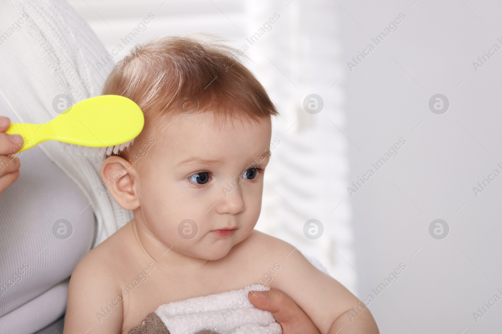 Photo of Woman brushing hair of her little baby indoors, closeup. Space for text