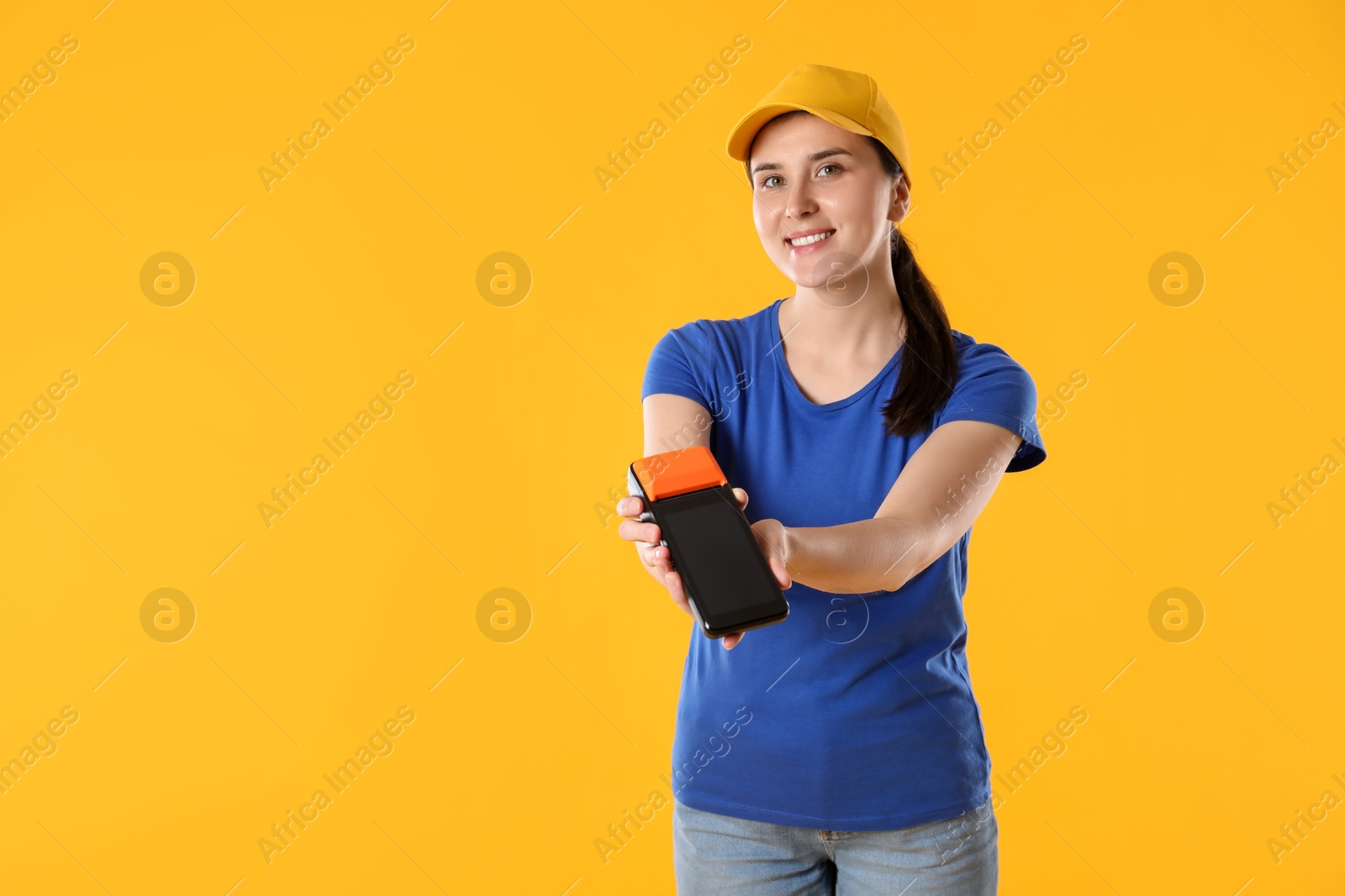 Photo of Happy courier with payment terminal on yellow background, space for text