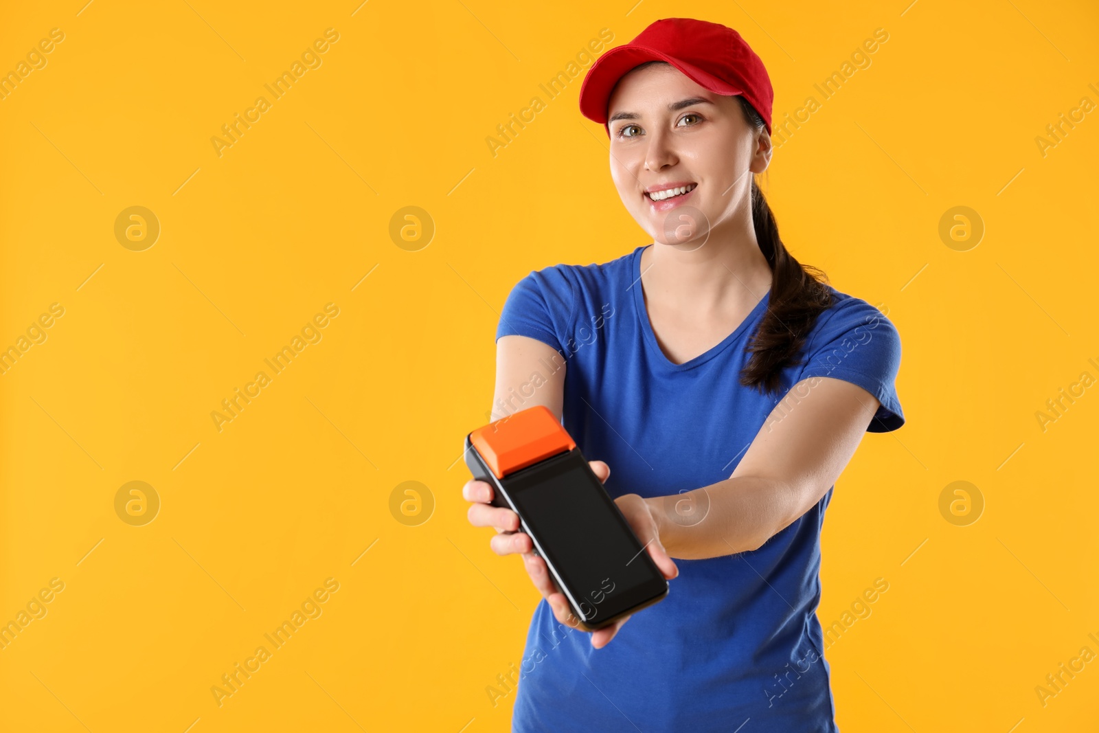 Photo of Happy courier with payment terminal on yellow background, space for text