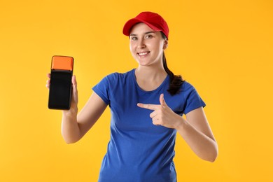 Photo of Happy courier with payment terminal on yellow background