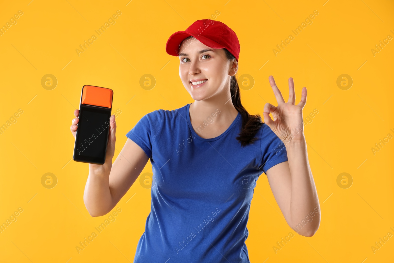 Photo of Happy courier with payment terminal showing OK gesture on yellow background