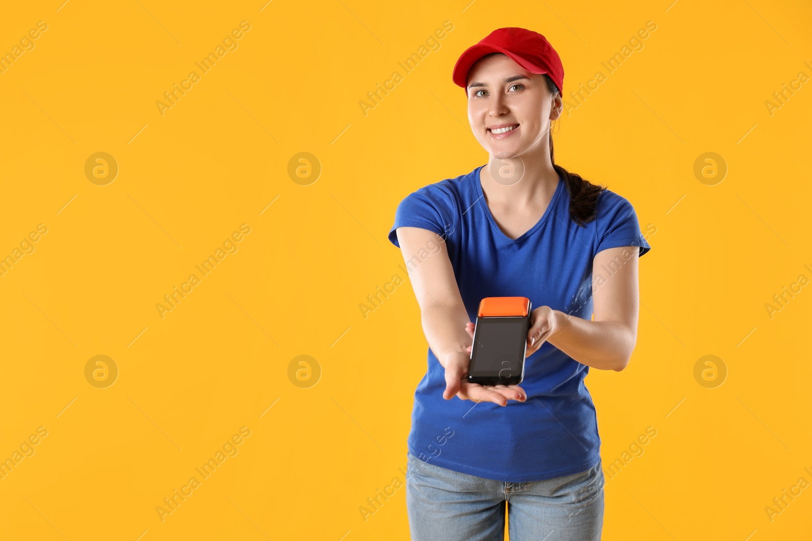 Photo of Happy courier with payment terminal on yellow background, space for text