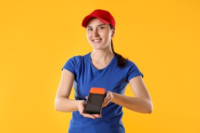 Photo of Happy courier with payment terminal on yellow background