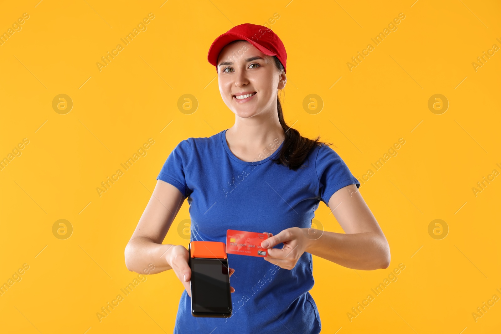 Photo of Happy courier with payment terminal and credit card on yellow background