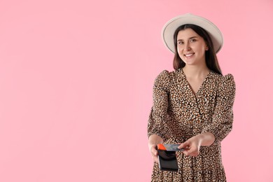 Photo of Happy young woman with payment terminal on pink background, space for text