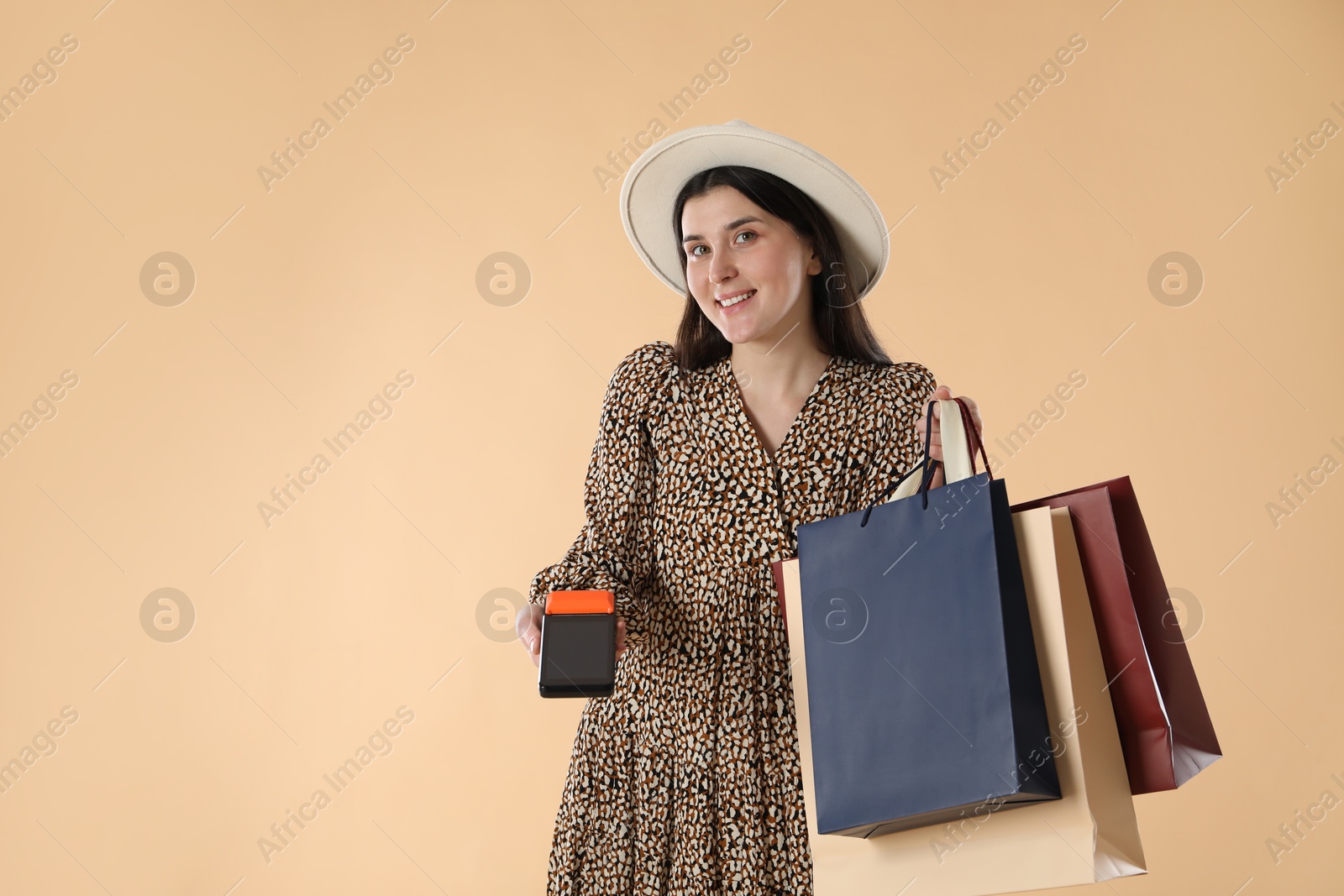 Photo of Happy young woman with payment terminal and shopping bags on beige background, space for text