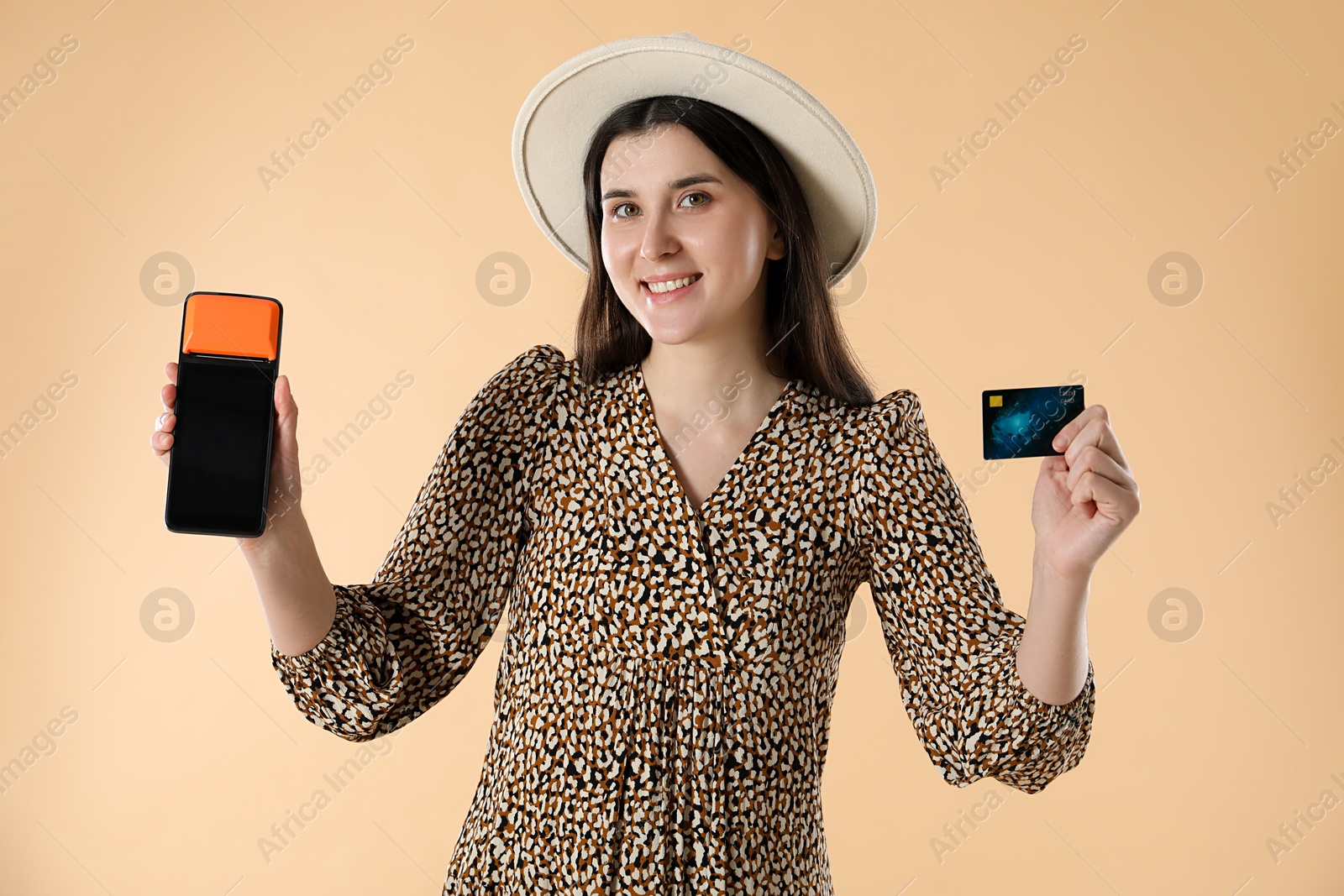 Photo of Happy young woman with payment terminal and debit card on beige background