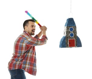 Photo of Emotional man hitting rocket shaped pinata with stick on white background