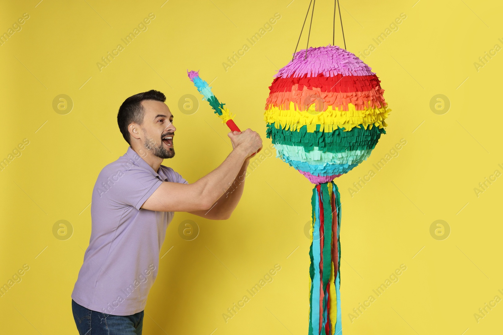 Photo of Emotional man hitting colorful pinata with stick on yellow background