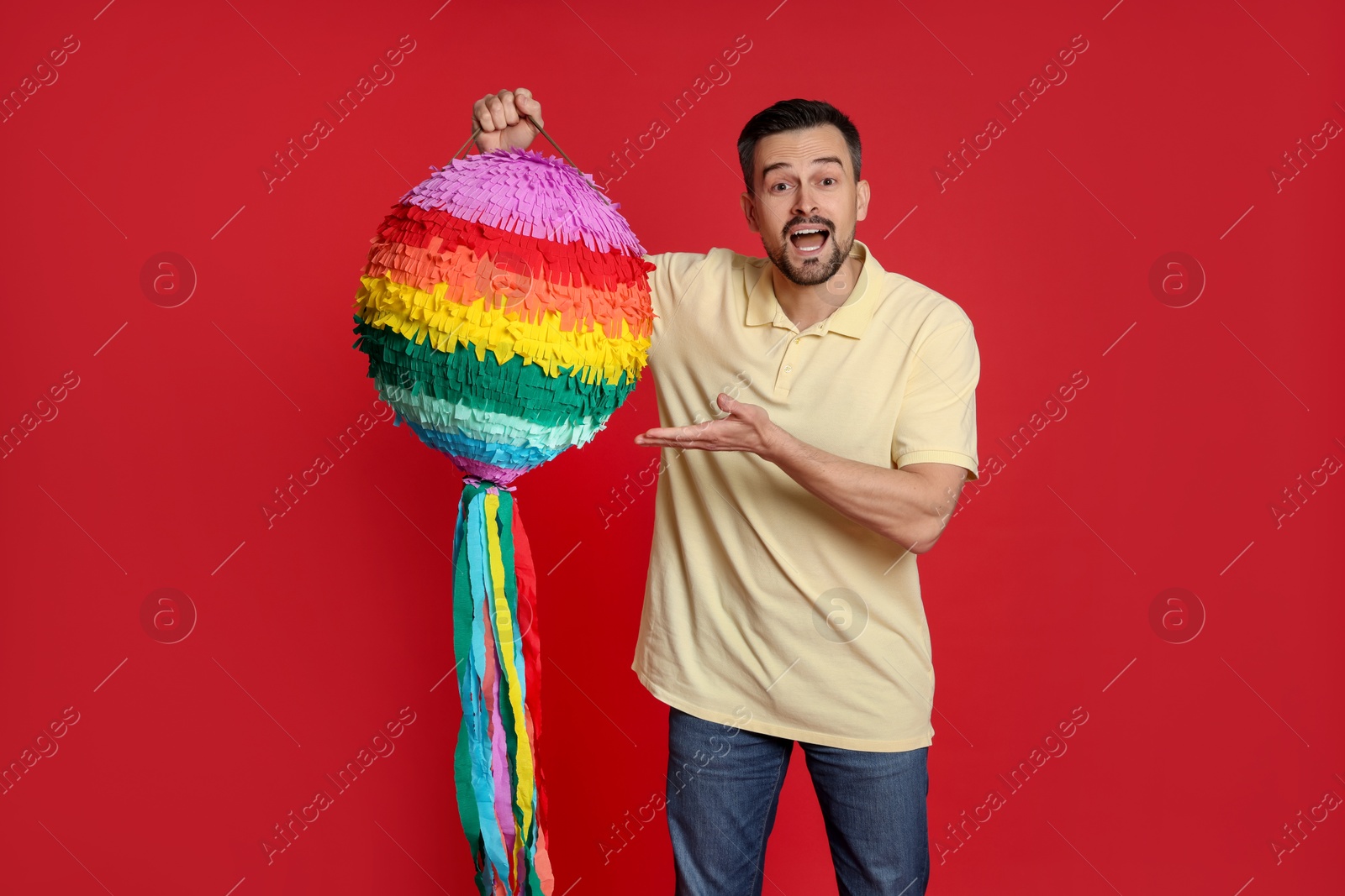 Photo of Emotional man with colorful pinata on red background