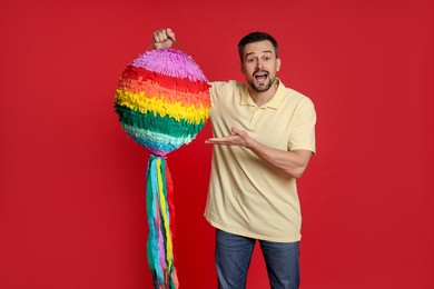 Emotional man with colorful pinata on red background